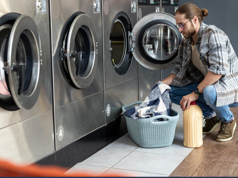 Adult man in self-service laundry shop operating coin washing machine to complete household chores